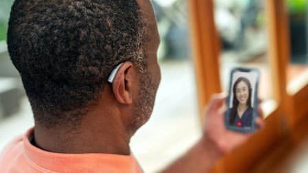 person wearing Lexie B2 Plus hearing aid while holding phone during video call