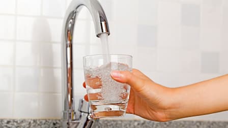 Hand holding a glass under a flowing kitchen tap.