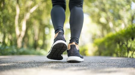 Closeup of the back of a person's shins and sneakers as they walk down a tree-lined paved road.