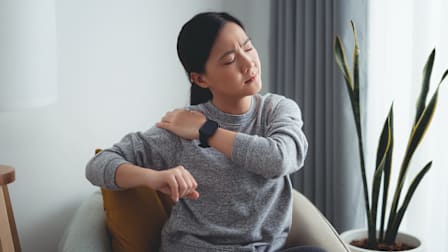 Person touching their shoulder and wincing in generic living room environment.