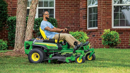 person riding John Deere Z330M-48 zero turn mower on lawn in front of brick house