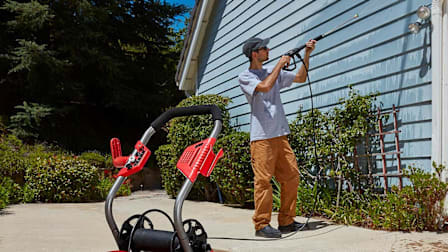 A man using a Bauer pressure washer to clean the siding on a house.
