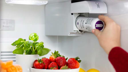 A hand installing a Whirlpool Everydrop filter  into a refrigerator filled with produce.
