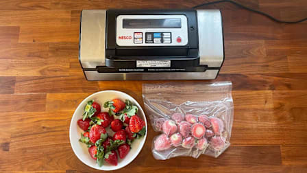 An overhead view of a vacuum sealer with a bowl of strawberries and a bag of vacuum sealed strawberries on a wooden kitchen counter.