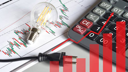 A lightbulb, power plug, and calculator on top of financial charts