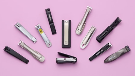 group of twelve various types of nail clippers on pink background