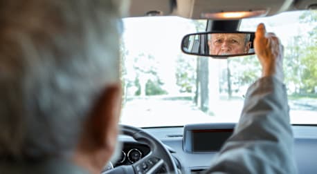 Older man looking in the rearview window of his car.