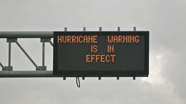A sign on the highway that says "Hurricane Warning is in Effect"