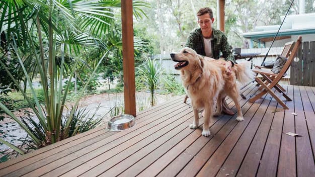 A person sitting at a table on a wood deck  while petting a dog