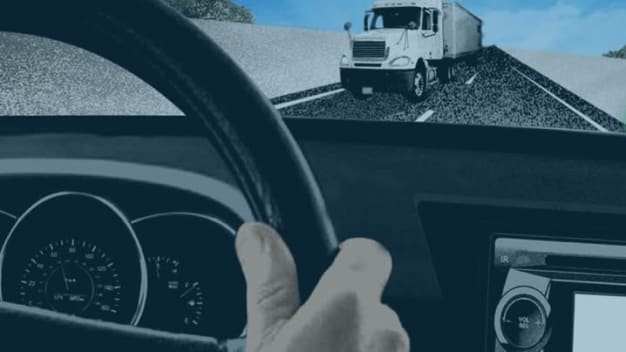 Driver's view through a car windshield with a tractor trailer on the road ahead.