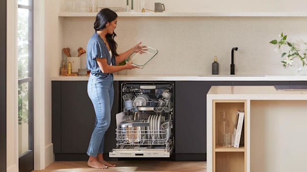 woman getting a clean dish from a Bosch dishwasher in kitchen with grey cabinets and open shelving