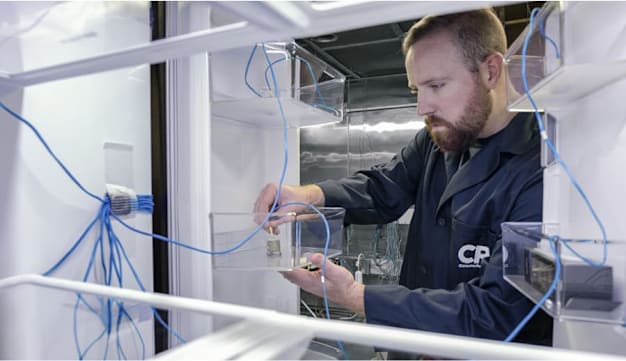 A CR tester is viewed from inside an open refrigerator, adjusting a temperature sensor