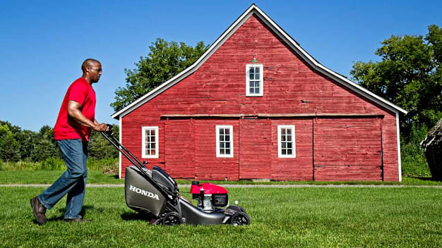 person using Honda HRN216PKA lawn mower with red barn and trees in background