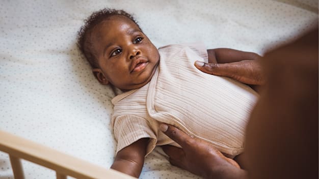 Black baby wearing a onesie being lifted from their crib by a caretaker.
