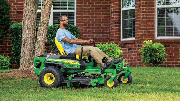 person riding John Deere Z330M-48 zero turn mower on lawn in front of brick house