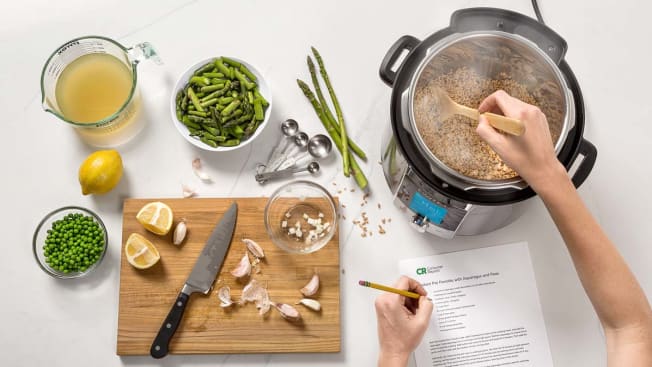 Person at kitchen counter with recipe and ingredients stirring Farrotto in an Instant pot.