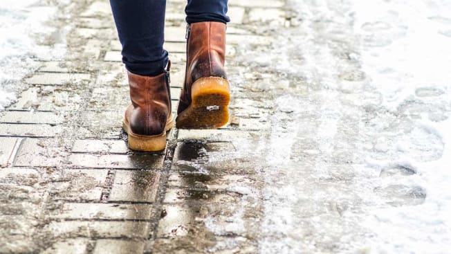 Close-up of a person wearing boots walking on an icy sidewalk