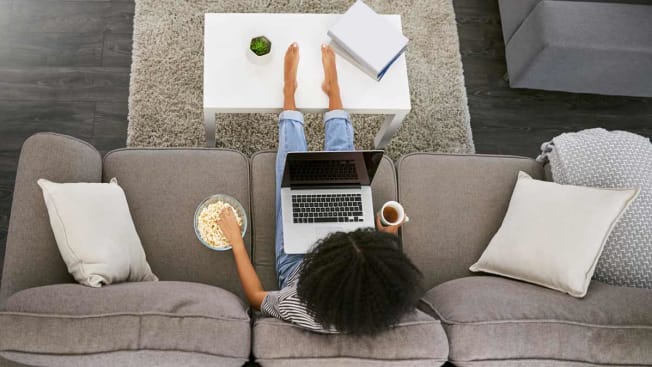 person using laptop on couch while eating popcorn