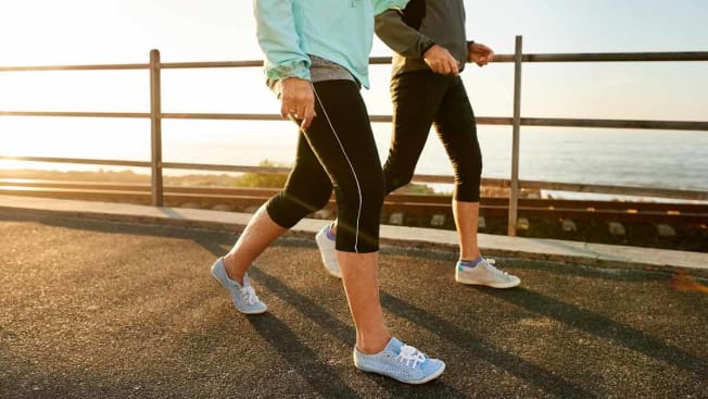 Two people walking on beach boardwalk wearing sneakers and fitness clothes