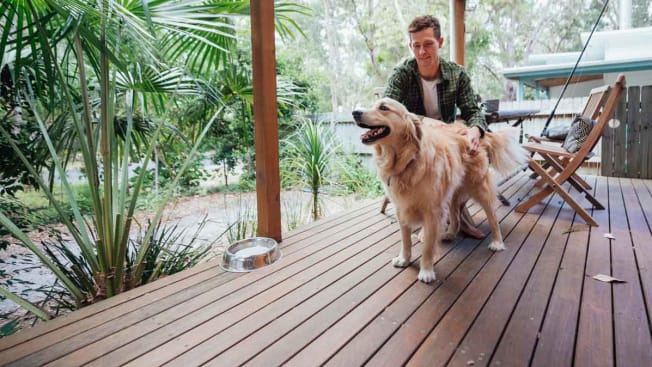 A person sitting at a table on a wood deck  while petting a dog