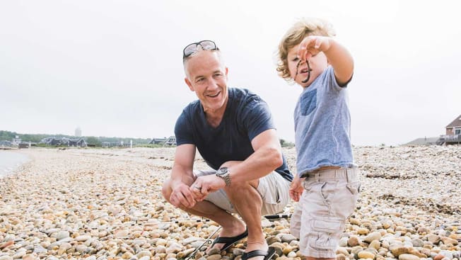 Senior adult with toddler on a beach during a cloudy day.
