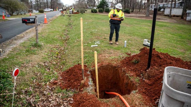 A technician checking the installment of fiber-optic cable that can be seen going through a large hole underground.