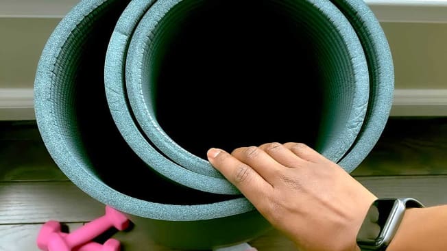 Person's hand touching a rolled up yoga mat.