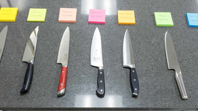 various chef knives lined up on counter with labels above them