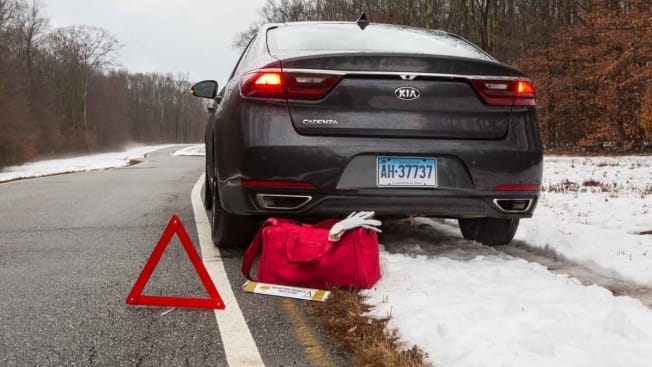 black car on side of wintery road with caution sign and emergency kit next to car