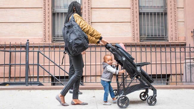 A woman pushes a stroller with a toddler on a city street.