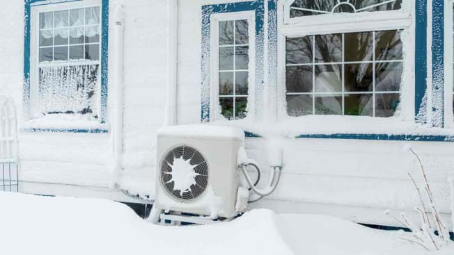 Heat pump covered in snow outside a house.