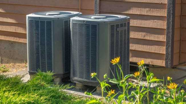 Two heat pumps sit outside a building to the side of green grass