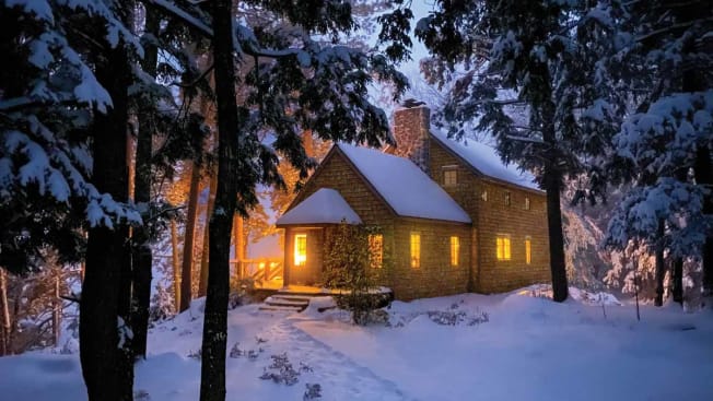 cedar shingled house at dusk covered in snow with snow covered evergreen trees