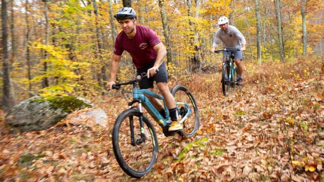 people riding HaiBike Hardnine 5.0 and Trek Powerfly 4 electric mountain bikes through wooded area