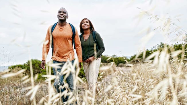 couple walking on path through field with ocean in background
