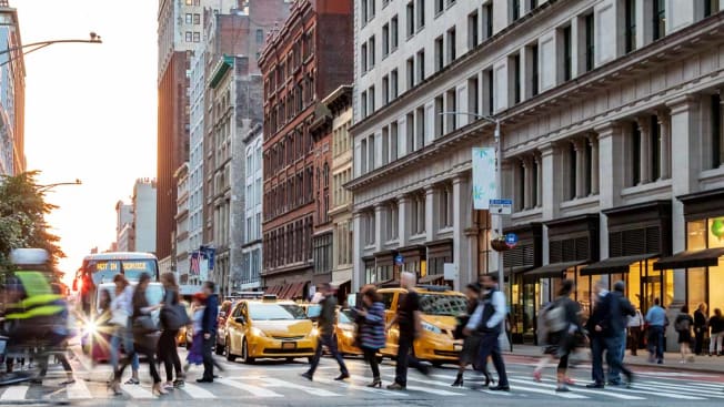 Multiple people walking across the street with cars stopped at a light in NYC