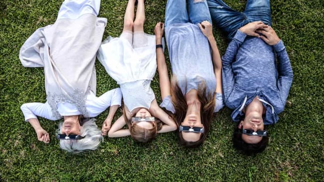 overhead view of family lying on grass with solar eclipse glasses