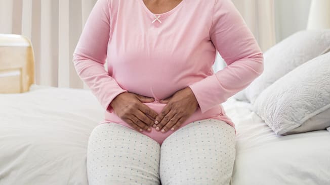 detail of person sitting on edge of bed holding stomach as though they're in pain