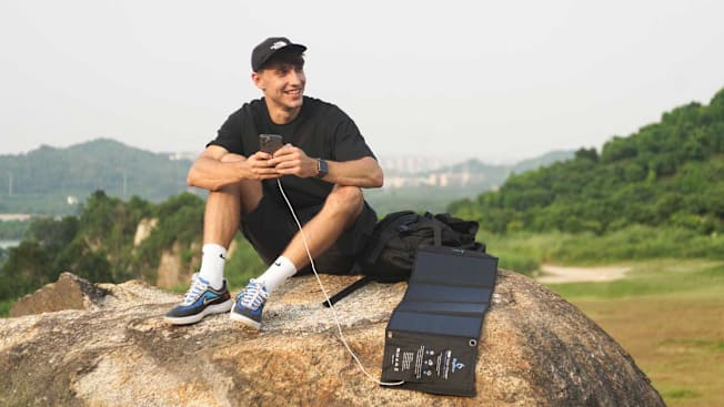 A person charging his phone using the BigBlue 28W Solar Charger while sitting outside