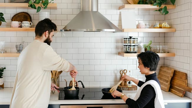 couple using cooktop with range hood and open shelving