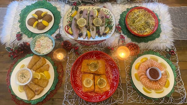 overhead view showing the seven dishes served during the Feast of Seven Fishes with lit candles and other holiday decor
