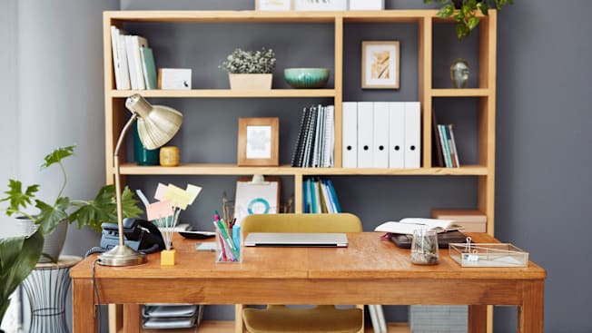 home office with wooden desk and chair, wooden bookshelf in background organized with documents, plants, and pictures