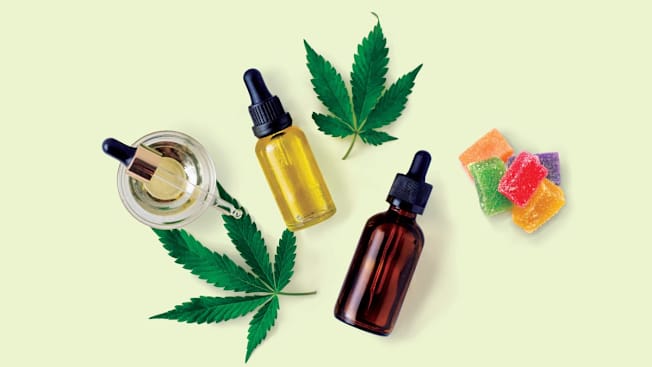 overhead view of various forms of cannabis (leaves, gummies, and oils) on light green background