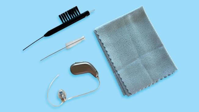 hearing aid, two different types of cleaning brushes, and microfiber cloth on blue background