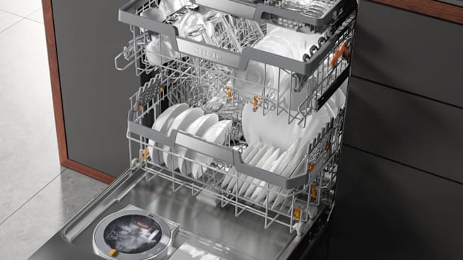 Miele G7176SCVI/G7176SCVI dishwasher open showing clean white dishes and glasses, dark grey cabinets on both sides