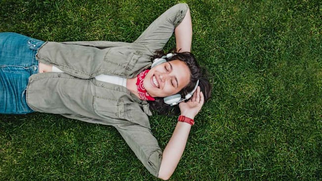 A woman lying on grass listening to audio from headphones.