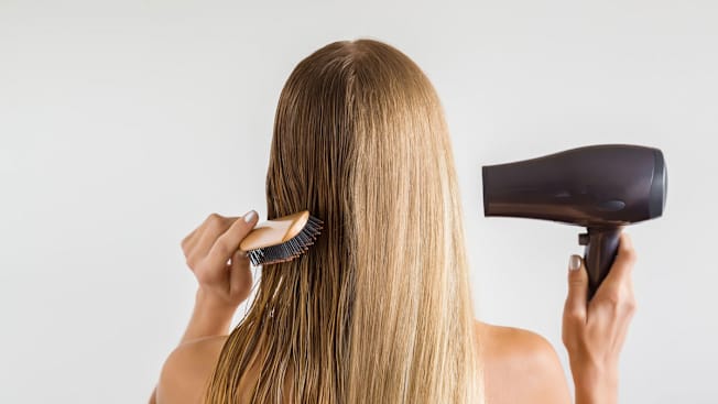 The back of a person's head with comb and hair drying in hands, drying and styling hair.