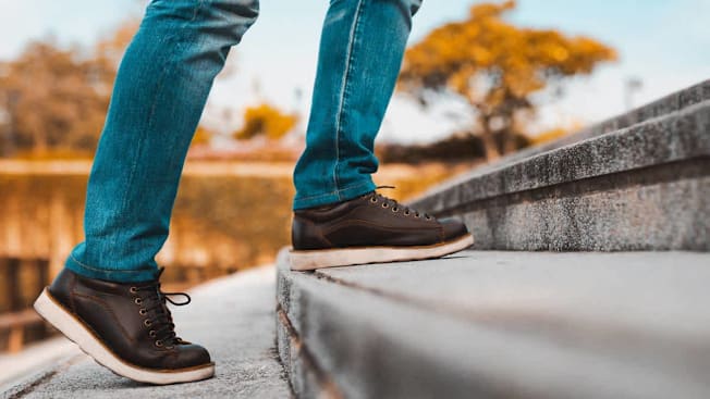 close up of person's feet and legs as they're walking up concrete steps with trees and sky in background