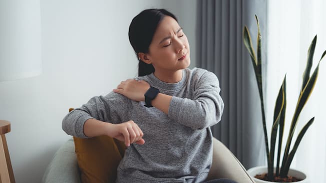 Person touching their shoulder and wincing in generic living room environment.