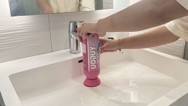 detail of person holding can of Yugou Foaming Drain Cleaner over bathroom sink